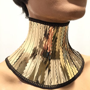 Op de afbeelding: Een gouden chokerketting met een gegolfde rand en zwarte bies. De ketting is gemaakt van metaal en heeft een reflecterend oppervlak.