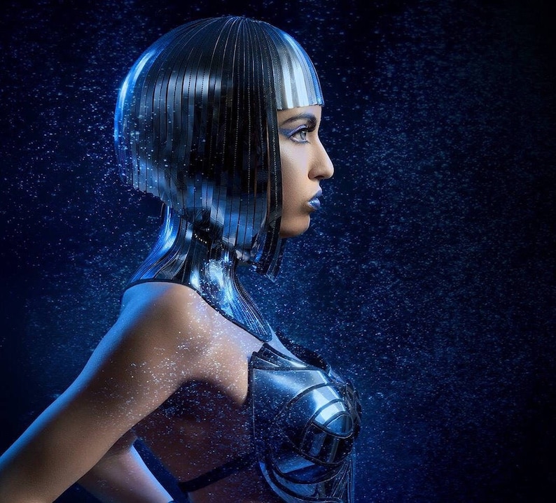 May include: A woman with a silver metallic bob haircut and a silver metallic bodice. The background is a dark blue with a light blue sparkle effect.