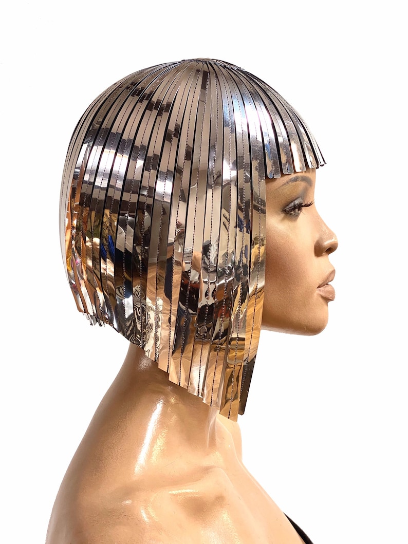 May include: A silver metallic wig with a short, blunt bob style. The wig is made of thin, flat strips of metal that are arranged in a layered fashion.