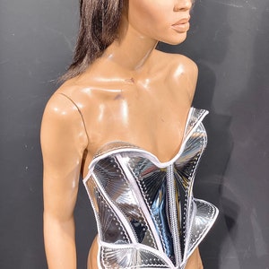 May include: A silver and white corset with a decorative design. The corset is made of a shiny, reflective material and has a white trim.