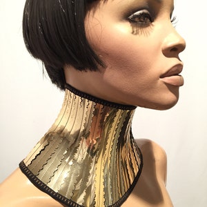 Op de afbeelding: Een gouden metalen choker ketting met een gegolfde rand en een zwarte stoffen achterkant.