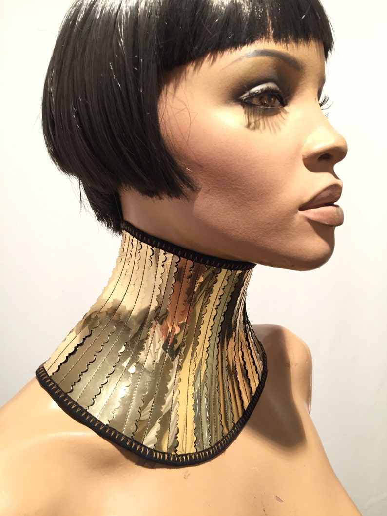 Op de afbeelding: Een gouden metalen choker ketting met een gegolfde rand en een zwarte stoffen achterkant.