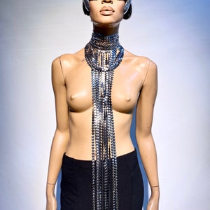 Op de afbeelding: Een zilveren en zwarte ketting met een zilveren masker op een mannequin.
