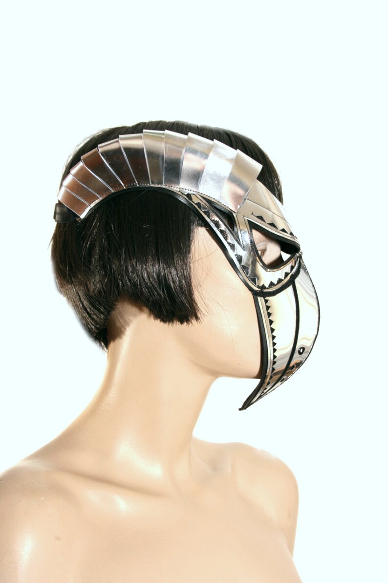 May include: A silver and black masquerade mask with a geometric design. The mask has a pointed chin and a large, open eye area.