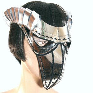 May include: A silver and black masquerade mask with a pointed beak and a decorative design. The mask is worn by a mannequin with black hair.