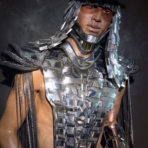 Pu&ograve; includere: Un costume argento e nero con un design a strati e frange. Il costume presenta un pezzo per il petto con un motivo geometrico e un grande collare d'argento.