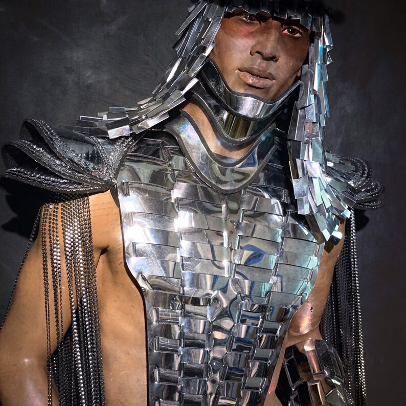 Pu&ograve; includere: Un costume argento e nero con un design a strati e frange. Il costume presenta un pezzo per il petto con un motivo geometrico e un grande collare d'argento.