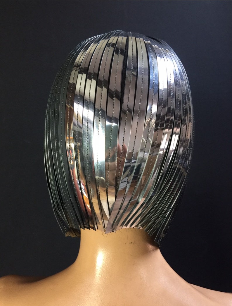 May include: A silver and black wig with a short, straight style. The wig is made of many thin strips of silver material that are sewn together.