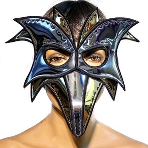 May include: A silver and black masquerade mask with a long beak and a starburst design. The mask is made of a shiny, reflective material.