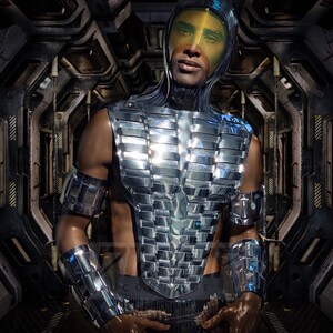 Pu&ograve; includere: Una persona che indossa un costume futuristico argentato, segmentato, con un casco giallo. Il costume ha un design geometrico ed &egrave; riflettente.