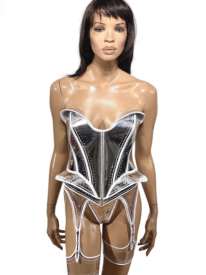 May include: A silver and white corset with a white lace trim. The corset has a sweetheart neckline and a boned structure. The corset is paired with a matching garter belt and stockings.
