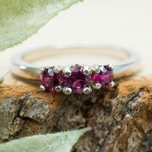 May include: A silver ring with three pink gemstones set in a row.
