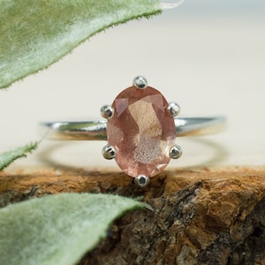 May include: A silver ring with a pink sunstone gemstone. The ring is set with a prong setting and has a polished finish.