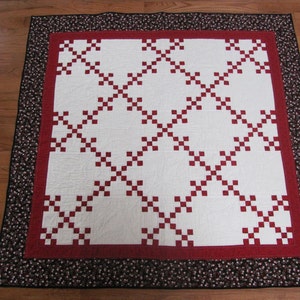 May include: A white quilt with a red diamond pattern and a black and white floral border.
