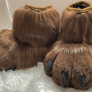 May include: A pair of brown furry slippers with black claws. The slippers are made of soft, plush fabric and have a realistic paw design.