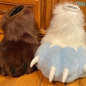 May include: Two furry paw-shaped hand puppets, one brown with black claws labeled "Slim" and one white with blue claws and a white tip labeled "Stompy".