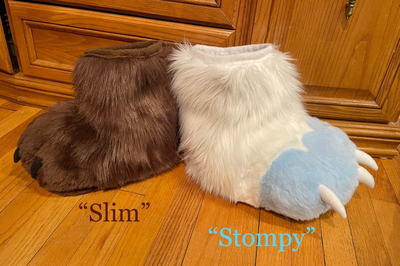 May include: Two pairs of fuzzy animal paw slippers. The brown pair is labeled "Slim" and the white pair with blue paw pads is labeled "Stompy".