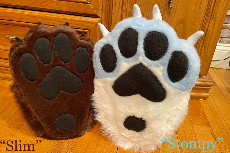 May include: Two plush paw-shaped hand puppets, one brown with black paw pads labeled "Slim" and one white with blue accents and black paw pads labeled "Stompy".
