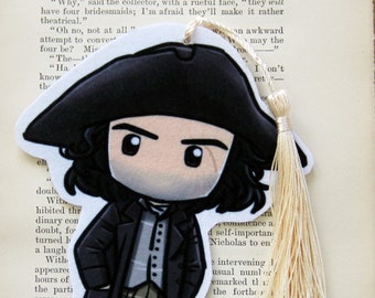 May include: A black and white illustrated bookmark featuring a cartoon character with a black hat, black hair, and a white shirt. The character is wearing a black jacket and brown pants. The bookmark has a white tassel.