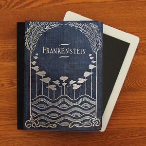 May include: A blue book cover with a silver design of waves, trees, and the title "Frankenstein". The book cover is on top of a white tablet.
