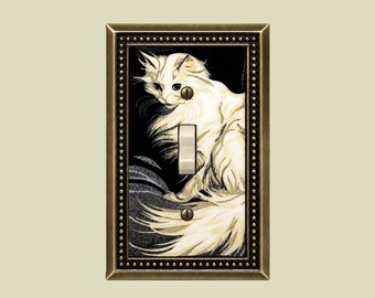 May include: A rectangular light switch plate featuring a decorative bronze-toned frame with a beaded border. The center panel displays a detailed illustration of a long-haired white cat against a dark background, with a central toggle switch.