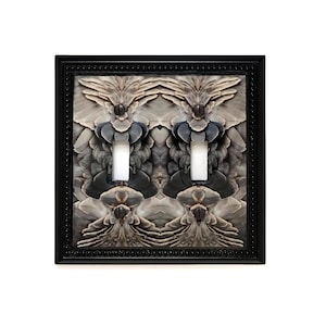 May include: A decorative double light switch cover with a black frame. The cover features a symmetrical design of gray and white feathers. The light switches are white.