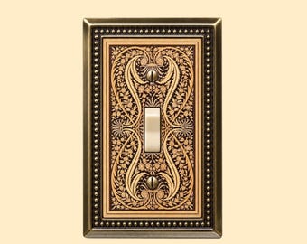 May include: A rectangular light switch plate featuring an antique brass finish with a beaded border. The center panel displays a dark brown background with an intricate, symmetrical gold-toned floral and vine pattern. A cream toggle switch is centered.