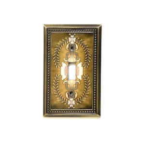 May include: An antique-style light switch cover with a bronze finish. The cover features a rectangular shape with a beaded border and a central floral design. The switch opening is white.
