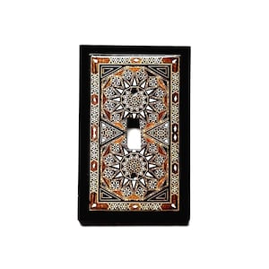 May include: A rectangular light switch plate featuring a dark black border and a central inlay design of geometric star patterns in shades of brown, black, and white. The plate has a centered vertical rectangular cutout for a toggle switch.