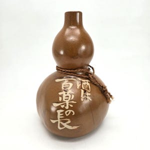 May include: A brown ceramic gourd-shaped vase with a rope tied around the neck. The vase has white Japanese characters on the side that read "真澄酒"