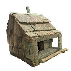 May include: A rustic, wooden birdhouse with a weathered appearance. The birdhouse features a shingled roof, a small porch, and a chimney. The wood has a natural, aged look with shades of brown and green, suggesting outdoor use.