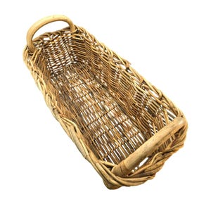 May include: A rectangular woven wicker basket featuring a natural light brown finish, an open top, and two sturdy arched handles positioned at each end. The basket is constructed with a visible interlaced pattern of thin, flexible wooden reeds.