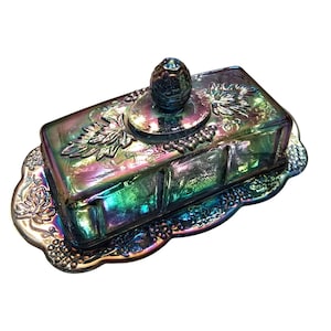 May include: Iridescent glass butter dish with a rectangular lid and a decorative base. The lid features a knob and grape vine detailing. The dish has a colorful, shimmering finish with shades of green, purple, and blue.