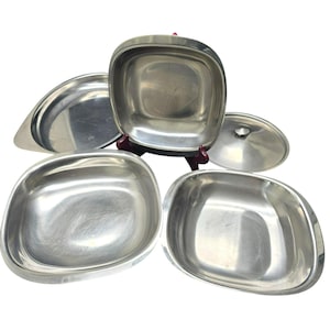 May include: Set of five silver serving dishes, including a lid. The dishes are round and oval shaped, with a shiny, reflective surface.
