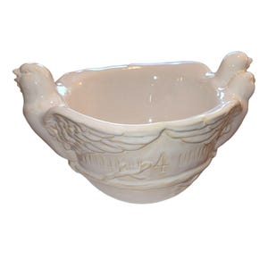 May include: Off-white ceramic bowl with a bird design. The bowl features two birds on either side, with wings forming the sides of the bowl. The base of the bowl has the number "4" and other text. The bowl is a decorative piece.
