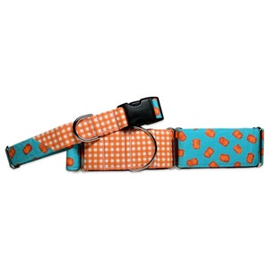 May include: A turquoise and orange dog collar with a checkered pattern and a print of orange nuggets on a turquoise background. The collar has a black buckle and a silver ring.
