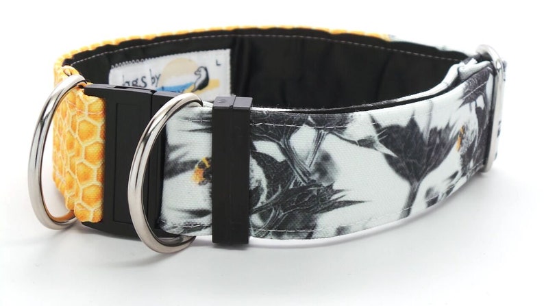 May include: A black and white dog collar with a honeycomb pattern on one side and a floral pattern on the other. The collar has a black buckle and two silver D-rings.