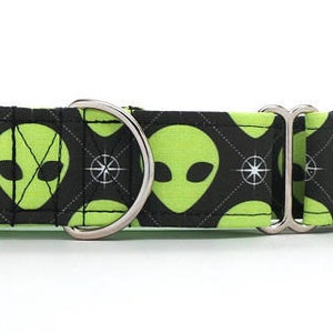 May include: A black and green dog collar with a repeating pattern of green alien faces and white compass designs. The collar has a silver buckle and a silver D-ring.