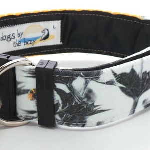 May include: A black and white dog collar with a yellow honeycomb pattern on one side and a black and white floral pattern on the other side. The collar has a black buckle and a silver D-ring. The collar is labeled "dogs by the bay".