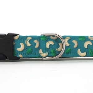 May include: A teal blue dog collar with a white cashew pattern and green leaves. The collar has a black plastic buckle and a silver metal D-ring.