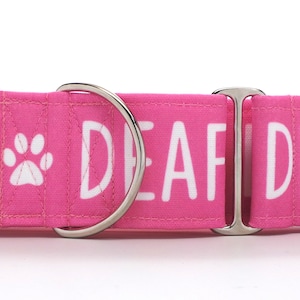 May include: Pink dog collar with white text that reads "Deaf" and a paw print. The collar has a silver buckle and a silver D-ring.