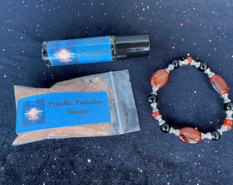 May include: A set of three items for psychic protection: a brown glass bottle with a silver cap labeled "Psychic Protection Oil", a small clear bag containing brown incense labeled "Psychic Protection Incense", and a red and black beaded bracelet.