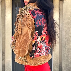 May include: Brown suede jacket with metal studs and a graphic print on the back. The jacket is paired with a red dress, fishnet stockings, and black boots. The jacket has a unique, edgy style.