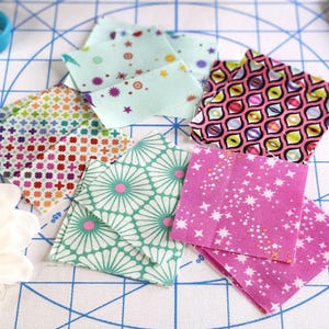 May include: A selection of patterned fabric squares in various colours, including pink, green, and multi-coloured designs. The squares feature star, flower, and geometric patterns, suitable for quilting or craft projects.