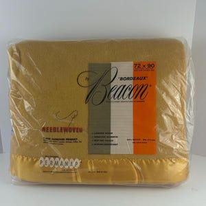 May include: A gold needlewoven blanket with a satin trim. The blanket is packaged in plastic and labeled "Beacon" "Bordeaux" 72 x 90. The label also states "A new improved product" and lists features like "Longer Wear", "Greater Warmth", "Softer Touch", and "Shrink-Resistant".