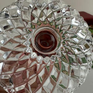 K&ouml;nnte beinhalten: Eine klare Glasschale mit einem ausgepr&auml;gten Diamantschliffmuster auf der Oberfl&auml;che. Das Design besteht aus sich wiederholenden geometrischen Facetten, die von einem glatten, kreisf&ouml;rmigen Mittelpunkt ausgehen und eine texturierte Optik erzeugen.