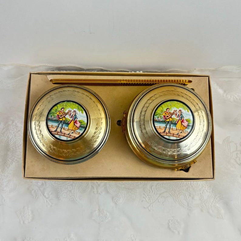 May include: Two vintage, round, gold-toned metal containers with a painted scene of a couple with a guitar. The containers are in a cardboard box. The lids have a textured design and a painted scene of a man playing a guitar and a woman dancing.