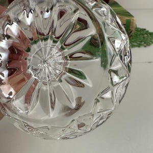 K&ouml;nnte beinhalten: Eine klare Glasschale mit einem facettierten, geometrischen Diamantschliffmuster an den Au&szlig;enseiten und einem strahlenf&ouml;rmigen Sternmuster, das von der Mitte des Bodens ausgeht und eine reflektierende und strukturierte Oberfl&auml;che erzeugt.