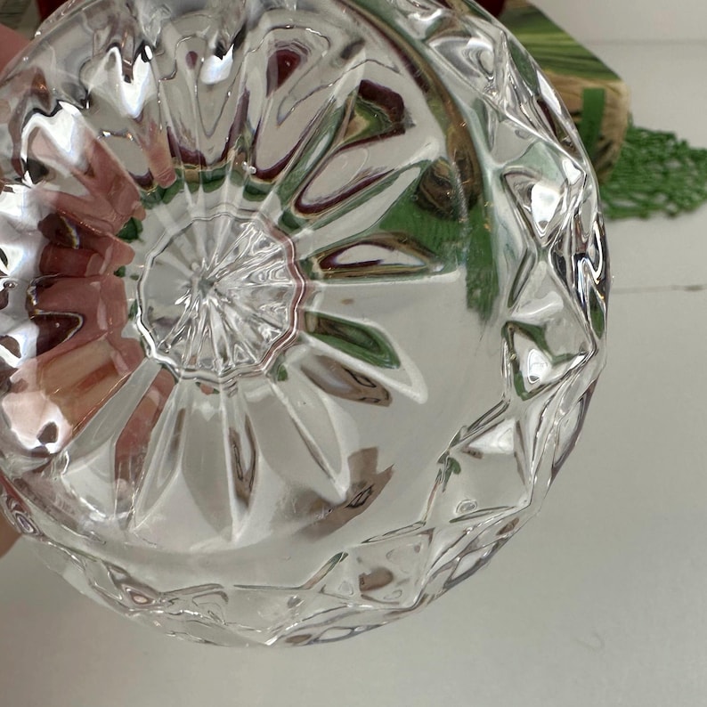 K&ouml;nnte beinhalten: Eine klare Glasschale mit einem facettierten, geometrischen Diamantschliffmuster an den Au&szlig;enseiten und einem strahlenf&ouml;rmigen Sternmuster, das von der Mitte des Bodens ausgeht und eine reflektierende und strukturierte Oberfl&auml;che erzeugt.