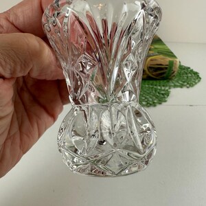 K&ouml;nnte beinhalten: Eine klare Glasvase mit einem facettierten Diamantschliffmuster auf der Oberfl&auml;che. Die Vase hat einen ausgestellten Rand, einen schmalen Hals und einen abgerundeten, bauchigen Fu&szlig;. Das Glas ist transparent und bricht das Licht.